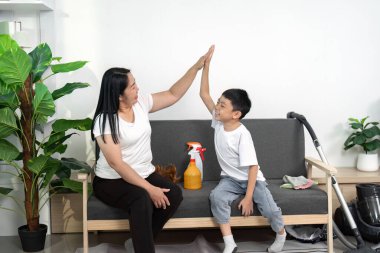 Ebeveynler ve çocuklar temizlik görevlerini tamamladıktan sonra beşlik çakar, ev işlerinde takım çalışması ve eğlenceyi vurgularlar.