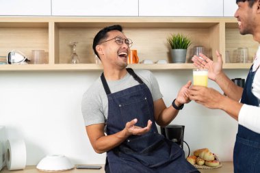 İki adam kadehlerini içkilerle kaldırırken neşeli bir anı paylaşıyor, çağdaş bir mutfakta bağlantı ve mutluluğu vurguluyorlar..