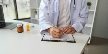 Modern bir muayenehanenin panosuna reçete yazan beyaz önlüklü bir doktor, hasta bakımını ve ilgiyi vurguladı..