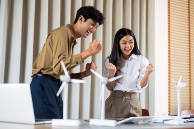 İki profesyonel, başarılı proje sonuçlarını yenilenebilir enerji odaklı parlak ve modern bir çalışma alanında kutlayarak heyecan ve neşe ifade ediyorlar..