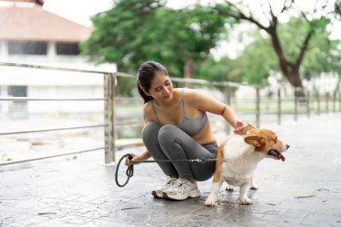 Korgisiyle yerde oturan bir kadın, açık hava aktiviteleri sırasında evcil hayvan bakımı ve sağlığın neşesini vurguluyor..