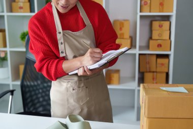 Organize bir çalışma alanında girişimci, teslimat için paketleri hazırlarken notlar alıyor ve envanteri yönetiyor.
