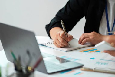 Bir iş toplantısında tablolar ve notları analiz eden iki meslektaş, mali stratejiler ve işbirliği üzerinde yoğunlaşıyor.