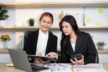 Çağdaş bir ofiste, iki iş kadını mali raporları gözden geçirir ve başarı stratejileri üzerinde işbirliği yaparlar..