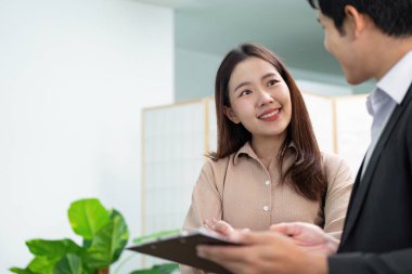 Neşeli bir emlakçı ve bir müşteri, parlak bir ofis ortamında potansiyel mülkler hakkında dostça bir sohbete girişiyor..