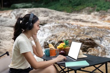 Bir kadın dışarıda bilgisayarını kullanırken gülümsüyor, dijital göçebe yaşam tarzını kucaklıyor..