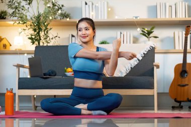 Bir kadın yoga minderinde oturur, kollarını dingin bir ev ortamında uzatır, esnekliği ve sağIığı teşvik eder..