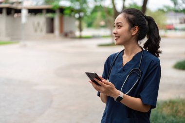 Bir sağlık uzmanı parkta akıllı telefonunu kontrol ederken gülümsüyor, modern sağlık hizmetleri iletişimini somutlaştırıyor..