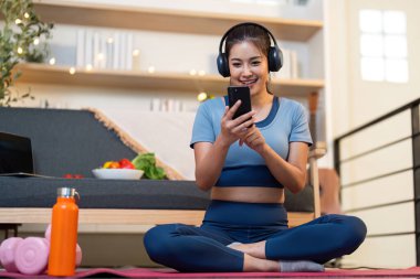 Bir kadın evde yoga yaparken akıllı telefonunu kullanıyor, teknolojiyi refahla harmanlıyor..