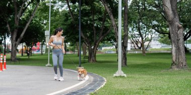 Bir kadın korgisini manzaralı bir park yolunda yürütür, açık hava aktivitelerini ve evcil hayvan arkadaşlığını ön plana çıkarır..