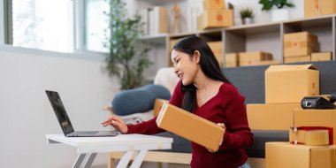 Bir kadın, ev ofis ortamında çoklu görev sergileyerek, telefonla teslimatları yönetir..