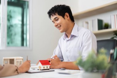 Bir emlakçı ve müvekkil, minyatür ev modelleri kullanarak mülkiyet seçenekleri hakkında tartışmaya girişirler..