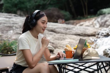 Bir kadın, açık havada çalışırken, sakin bir doğal ortamda uzaktan çalışmanın esnekliğini gösteren bir video görüşmesinden hoşlanır..