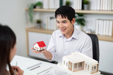 Bir emlakçı, profesyonel bir ortamda tasarım ve özellikleri vurgulayarak bir müşteriye model ev sunar..