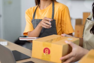 Eşleşen önlük giyen iki çalışan, küçük işletmelerdeki takım çalışmalarını vurgulayarak, paket teslimatlarını yönetmek için ortak bir çaba sarf ediyorlar..