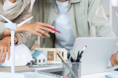 Dizüstü bilgisayar ve model kullanarak tasarım planları üzerinde işbirliği yapan mimarlar, takım çalışması ve yenilik sergiliyor.