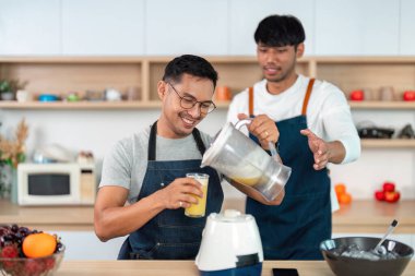 İki adam mutfakta birlikte çalışıyor. Lezzetli meyve suyu, takım çalışması ve neşe katmak için taze malzemeleri karıştırıyorlar..