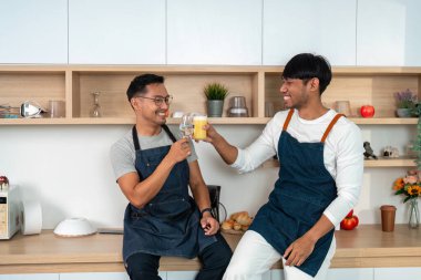 İki adam birlikte geçirdikleri zamanı şık bir mutfak ortamında bir bardak taze meyve suyuyla kadeh kaldırarak kutluyorlar..