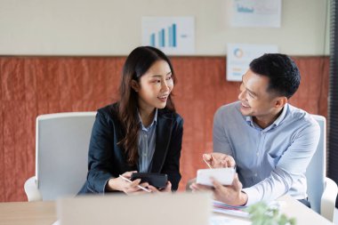 İki meslektaş, parlak bir ofis alanındaki belgeleri incelerken proje stratejileri hakkında canlı bir sohbete girişiyor.
