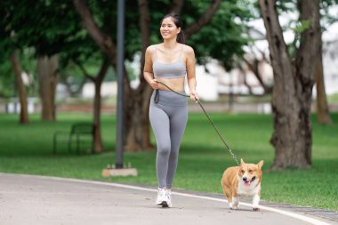 Bir kadın canlı bir parkta Corgi 'sini gezdirir, açık hava aktiviteleri ve neşeli arkadaşlık yoluyla sağlığını arttırır..