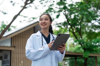 Bir doktor bir tablet tutuyor ve dışarıda dururken gülümsüyor, modern sağlık ve teknoloji entegrasyonunu temsil ediyor..