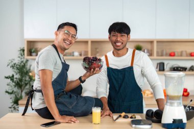 İki adam bir kase taze meyveyi şık mutfaklarında paylaşıyor, bağlarını ve sağlıklı yaşam tarzlarını vurguluyorlar..