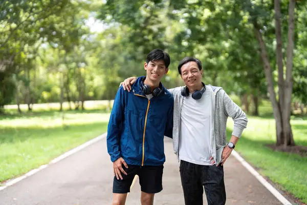 Genç bir adam ve yaşlı bir adam gülümsüyor ve dışarıda egzersiz yaptıktan sonra fotoğraf için poz veriyorlar, arkadaşlıklarını ve sağlıklarını gösteriyorlar..