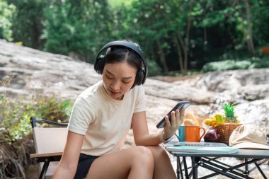 Açık havada akıllı telefonunu kullanırken yansıyan genç bir kadın, farkındalığı ve doğayla bağlantıyı vurguluyor..
