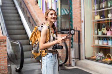 Genç bir gezgin yürüyen merdivenin yanında duruyor, akıllı telefonunu kullanarak şehir keşiflerinin tadını çıkarıyor..
