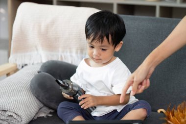 Elinde elektrikli süpürge tutan genç bir çocuk, kanepede otururken yaratıcı bir oyun oynuyor, oyun oynayarak öğrenmenin zevkini vurguluyor..