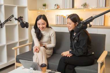 İki kadın bir podcast sırasında gülüp birbirlerine bağlanıyorlar, samimi bir stüdyoda işbirliği yapmanın sevincini vurguluyorlar..