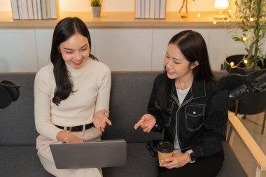 İki kadın bir podcast stüdyosunda canlı bir sohbete girişiyor, fikirleri ve kahkahaları paylaşıyorlar. Atmosfer sıcak ve kapsayıcı..