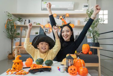 Neşeli bir anne ve oğul Cadılar Bayramı 'nı kutluyor, şenlikli şapkalar takıyor ve etrafı süslemeler, balkabakları ve el sanatlarıyla çevrili..