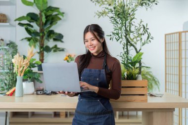 Bir kadın, bir fabrikada dizüstü bilgisayarıyla iletişim kuruyor, teknolojiyi bahçe işlerine olan tutkusu ile harmanlıyor..