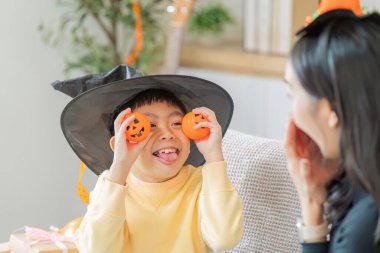 Cadılar Bayramı şenlikleri sırasında annesiyle neşeli bir anı paylaşan cadı şapkalı mutlu bir çocuk balkabağı oyuncakları tutuyor..