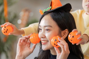 Bir kadın elinde balkabağı oyuncakları tutarken gülümserken oğlu Cadılar Bayramı kutlamalarında onunla şakalaşıyor..