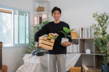 Genç bir adam elinde bir sandık çiçek ve saksı bitkisi tutuyor. Yaşam alanını yeşillik ve renkle genişletmeye hazır..