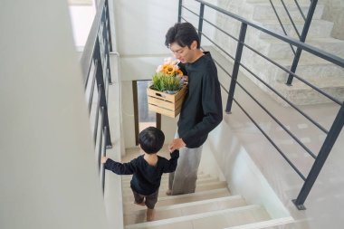 Bir baba ve oğul birlikte merdivenlerden aşağı iniyor, saksı bitkileri taşıyor, takım çalışmasını ve aile bağlarını sembolize ediyor.