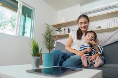 Bir anne ve oğlu video oyunları oynarken kanepede samimi bir anı paylaşıyor, sıcaklığı ve bağlantıyı vurguluyorlar..