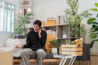 Genç bir adam, modern iletişimi yansıtan şık bir oturma odasında otururken bir telefon görüşmesi yapar..