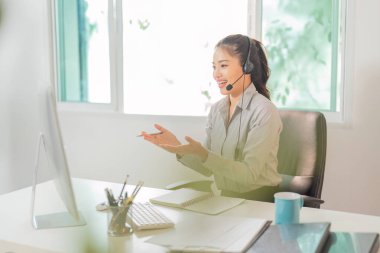 Neşeli bir bayan müşteri hizmetleri temsilcisi müşterileriyle modern bir çalışma alanında kulaklık kullanarak iletişim kuruyor..