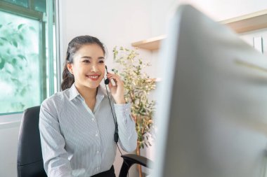 Kulaklıklı genç bir kadın sanal bir toplantıya katılırken gülümsüyor ve uzaktan çalışmanın özünü gözler önüne seriyor..