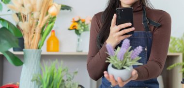 Genç bir kadın, bahçıvanlık tutkusu ile teknolojiyi harmanlayan, bir saksı lavanta bitkisini sergilerken akıllı telefonuyla meşgul oluyor..