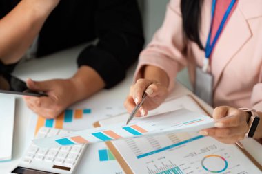 İş arkadaşıyla stratejileri tartışırken mali tablolara işaret eden bir kadın, veri analizi ve takım çalışmasına odaklanıyor.