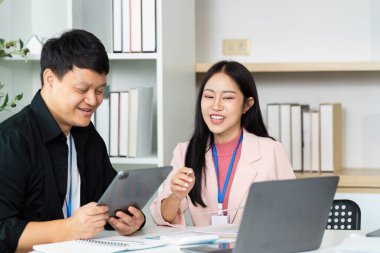 Bir tableti incelerken gülümseyen ve görüşleri paylaşan iki profesyonel, takım çalışmasını ve etkili iletişimi vurguladı.