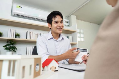 Bir emlakçı müşteriye bir emlak modeli gösteriyor, özellikleri vurguluyor ve potansiyel yatırımları tartışıyor.