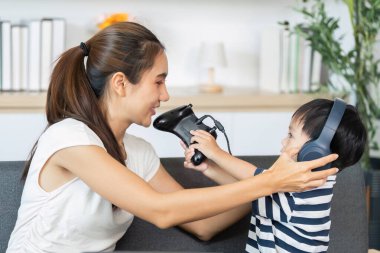 Bir anne ve oğlu oyun oynarken kulaklıklarını paylaşıyor, bir bağlantı anını gösteriyor ve sıcak bir ev ortamında keyif paylaşıyorlar..