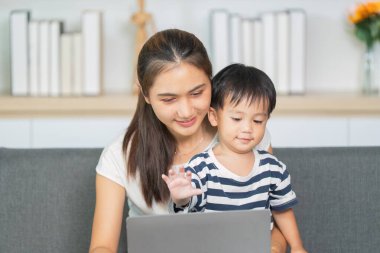 Neşeli bir anne ve küçük oğlu, rahat bir oturma odasında öğrenme ve iletişim anlarını paylaşan bir dizüstü bilgisayarla meşgul..