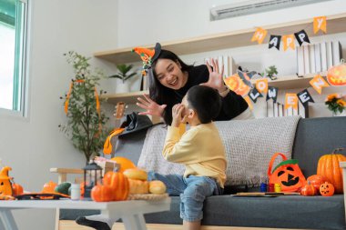 Bir anne ve oğlu Cadılar Bayramı için balkabağı ve şenlik dekorlarıyla dolu bir oturma odasında süsleme yaparken kahkahalarını paylaşıyorlar..