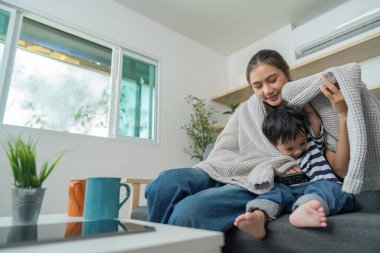 Bir anne ve oğlu kanepede sıcak bir anı paylaşıyor, battaniyeye sarılıp, sıcak bir oturma odasında kaliteli zaman geçiriyorlar..